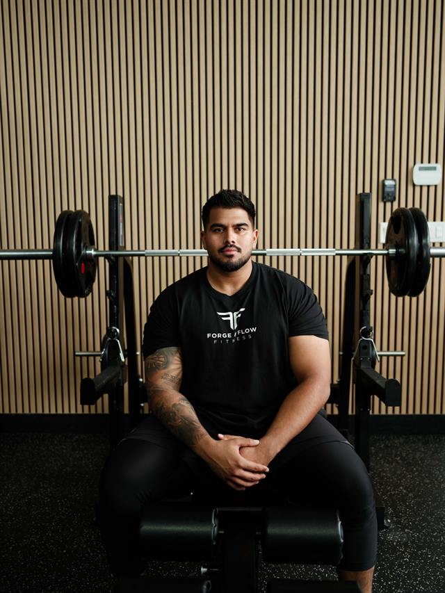 Coach Jayden Grewal seated in front of gym equipment